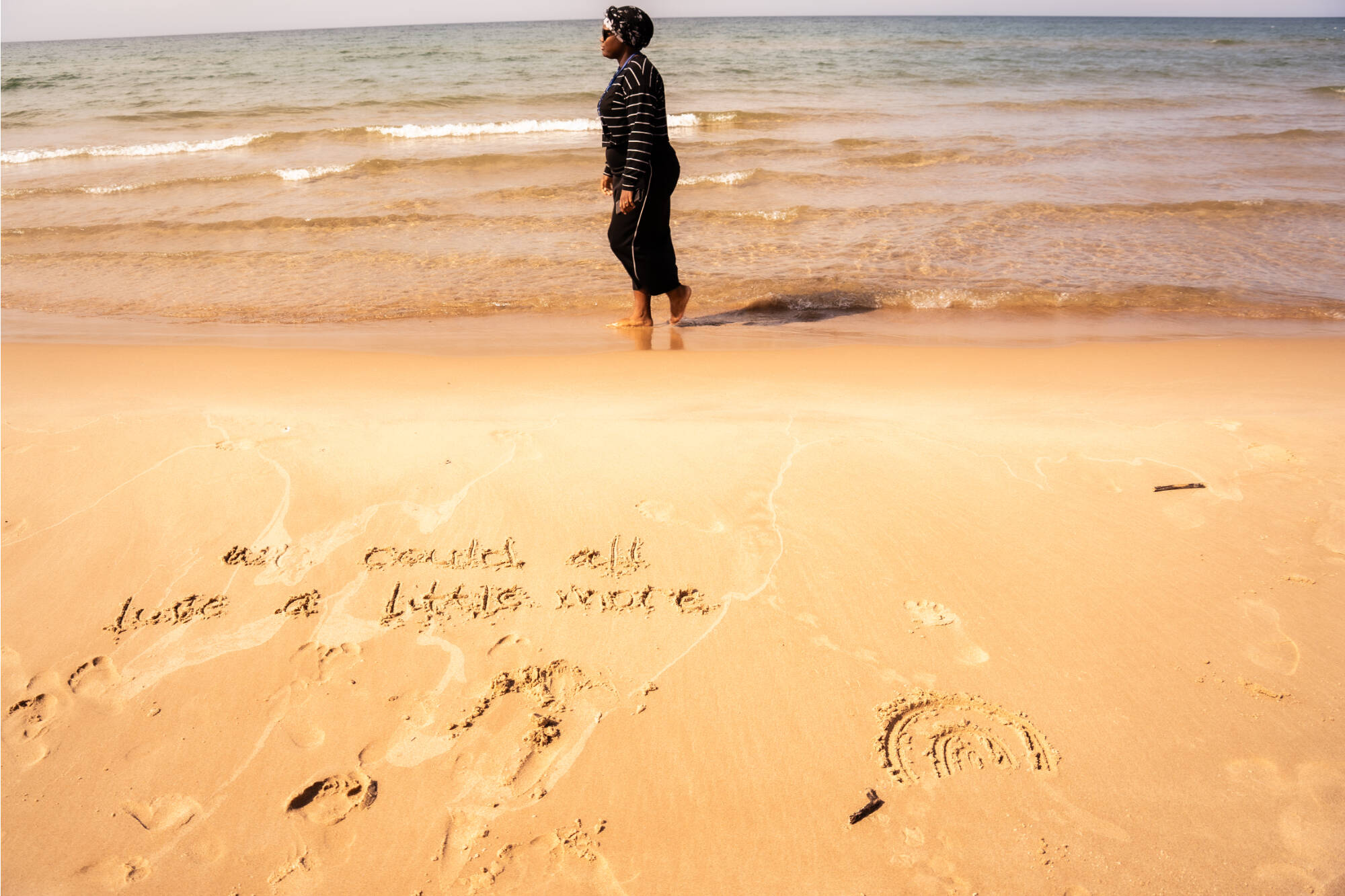 A student walking on the beach in the surf with "We could all love a little more" written in the sand